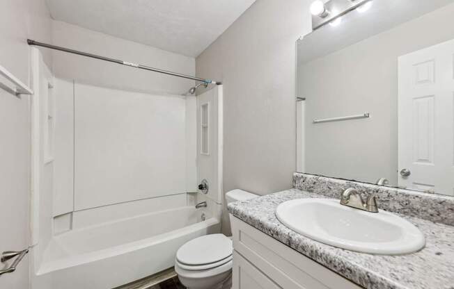 A white bathroom with a toilet, sink, mirror, and bathtub at Gwinnett Square Apartments in Duluth, GA