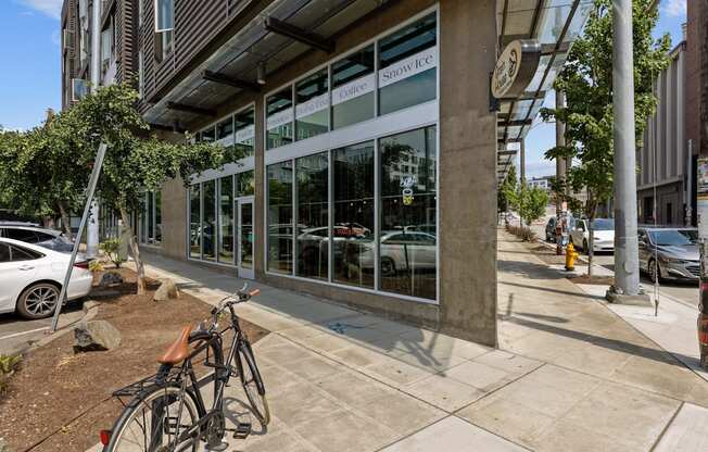 A bicycle is parked on the sidewalk in front of a building with a glass facade.