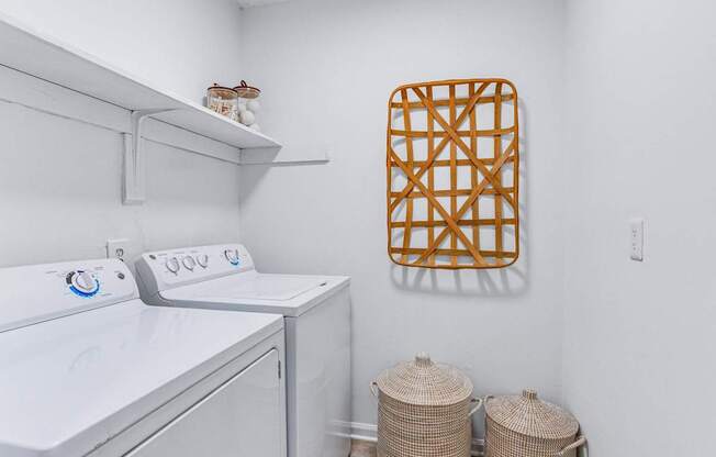 A laundry room with a washer and dryer, a basket, and a wall hanging.