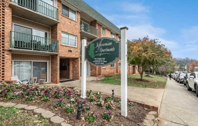 A sign for "Residential Apartments" stands in front of a brick building with a parking lot in the background.