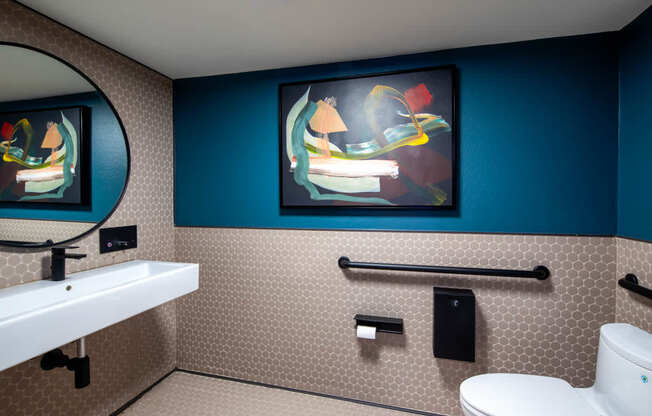 A bathroom with a toilet, sink, and a painting on the wall.