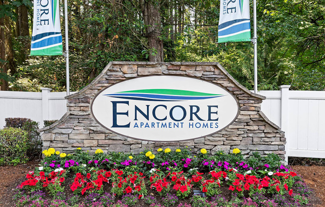 A sign for Encore Apartment Homes is surrounded by flowers.