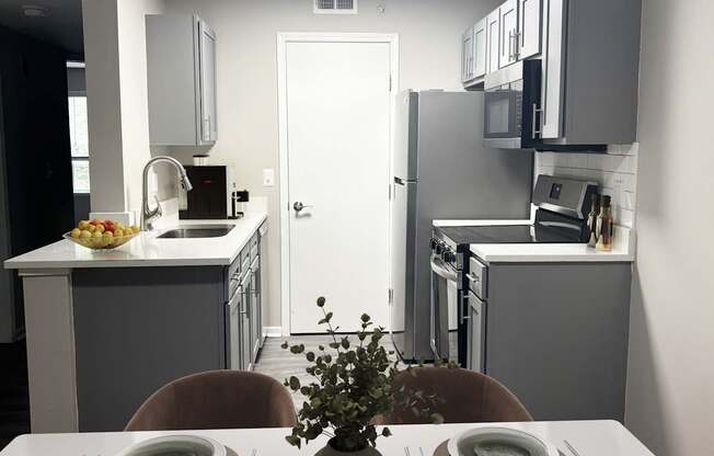 A dining table set with plates and cutlery is in the foreground of a modern kitchen.