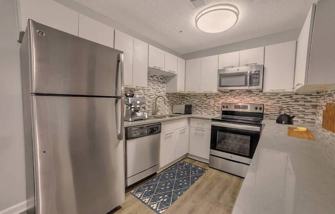 A kitchen with a stainless steel refrigerator and a stone backsplash.