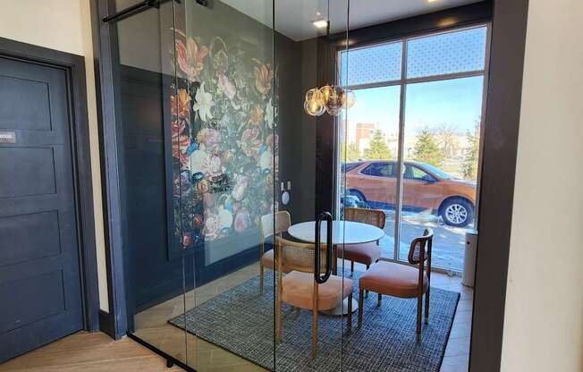A glass door with a black frame leads to a balcony with a table and chairs.