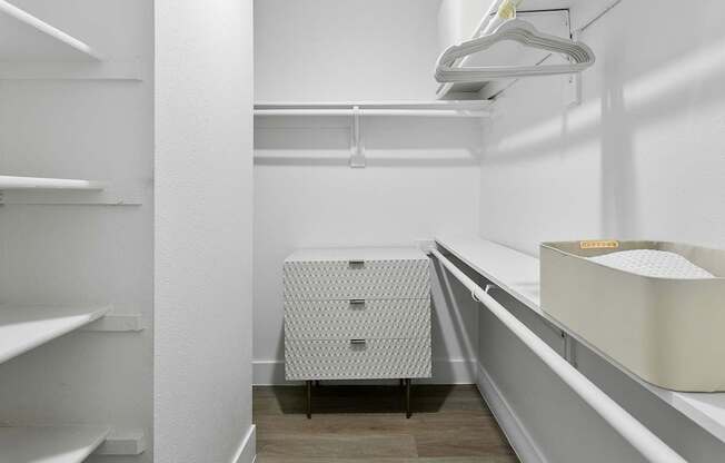 A walk-in closet with white shelves and a white dresser.