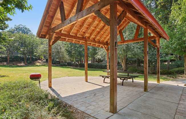 A wooden pavilion with a red roof is surrounded by greenery.