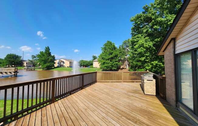 A wooden deck overlooks a body of water with a house and trees in the background.