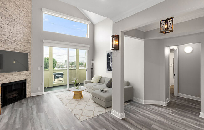 Hardwood floored living room with view of stone accent wall, fireplace, and high third-floor ceilings.