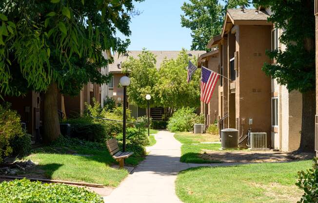 a pathway lined with green grass and trees in front of an apartment building at Oak Terrace Senior Apts, Hemet