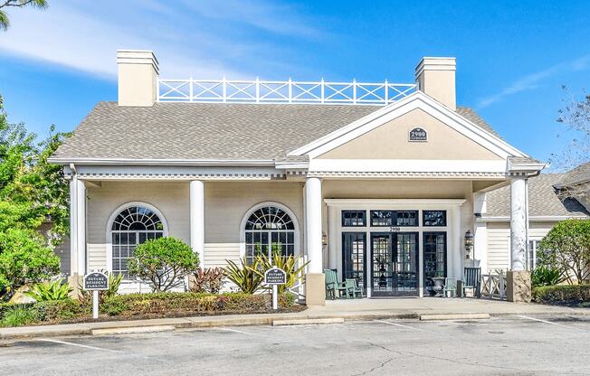 Clubhouse and leasing office exterior entryway with green rocking chairs, welcome mat, covered porch, and parking lot in front