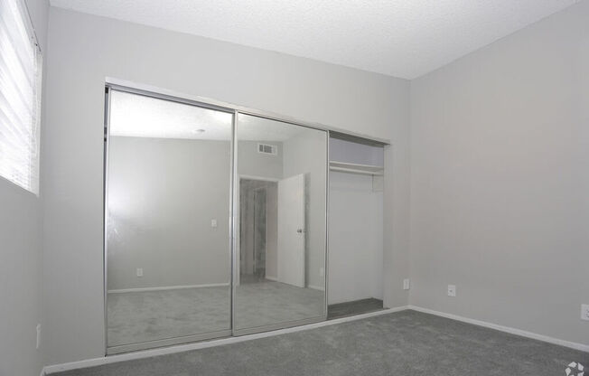 an empty living room with a large window and a mirrored closet  at The Marq Apartments LLC, Los Angeles, California