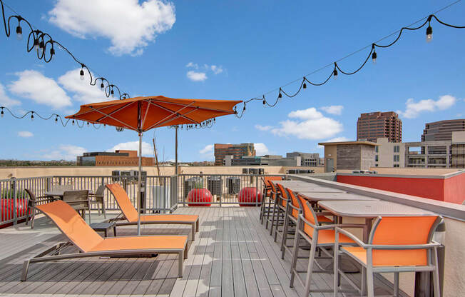 a rooftop deck with orange lounge chairs and umbrellas