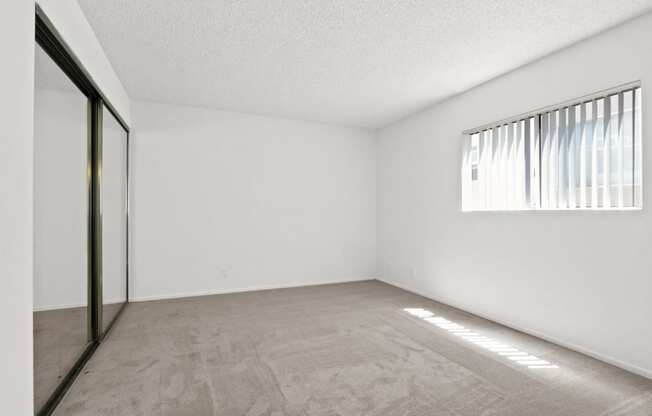 the spacious living room of an apartment with white walls and a window