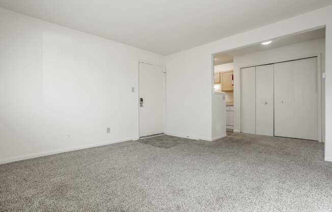 a living room with white walls and carpet and a door to a kitchen