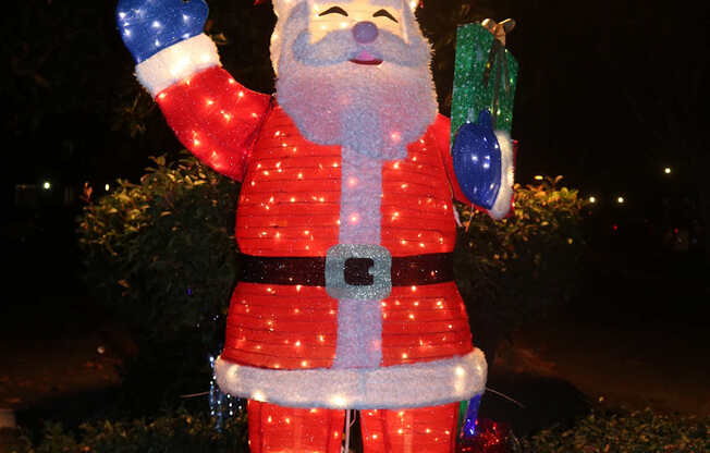 A lighted Santa Claus statue is standing in the grass.