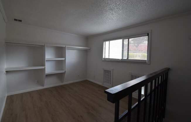 an empty living room with white shelves and a window