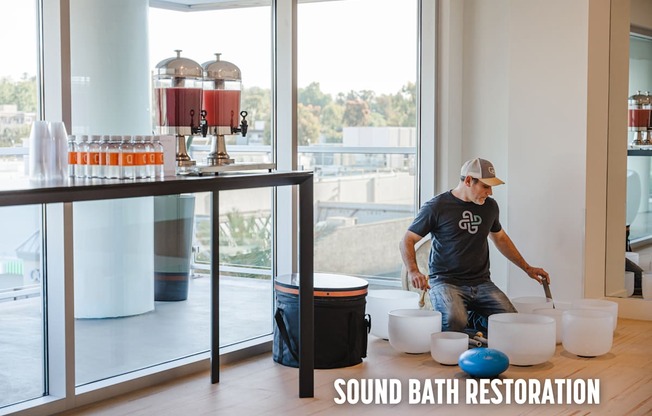 A man is working on a sound bath restoration setup in a room with large windows.