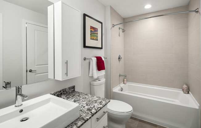 a bathroom with a white bathtub and a white sink with a granite countertop