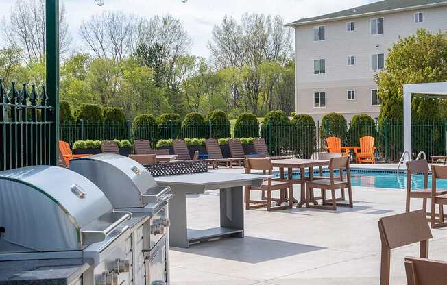 A patio with a grill, chairs, and a pool.