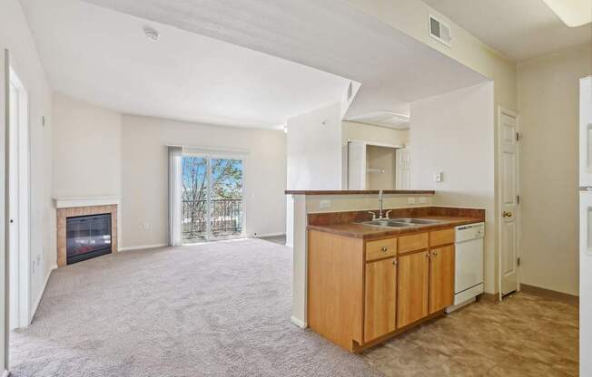 A spacious living room with a fireplace and a kitchen area with wooden cabinets and white appliances.