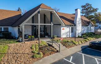 A white building with a brown roof and a black car parked in front.