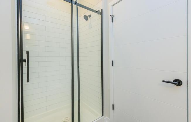 A modern bathroom featuring a glass-enclosed shower with black hardware, white tiled walls, and a sleek door. The interior conveys a clean and contemporary design aesthetic.