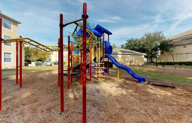 A playground with a red and yellow structure and a blue slide.