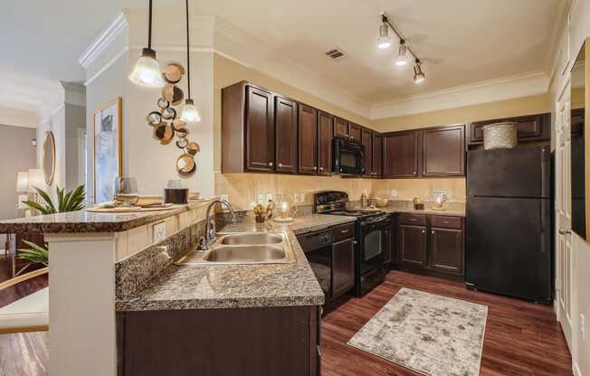 a kitchen with espresso color cabinets, granite countertops, designer lighting fixtures and black appliances