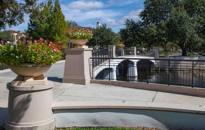 A bridge over a canal with a fence and a large planter with red flowers.