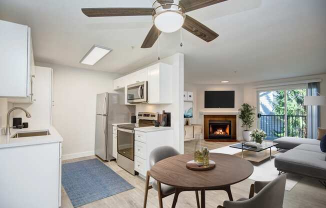 a kitchen and living room with a ceiling fan and a fire in the fireplace