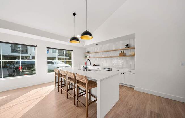 A modern kitchen with a white counter and wooden chairs.