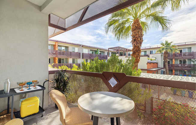 A balcony with a table and chairs overlooking a building with a palm tree.
