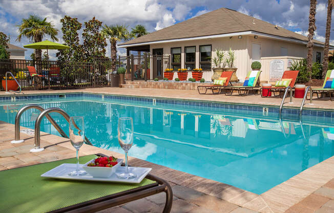 A poolside table with a plate of food and two glasses of wine.