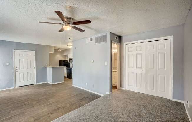 an empty living room with a ceiling fan and a kitchen