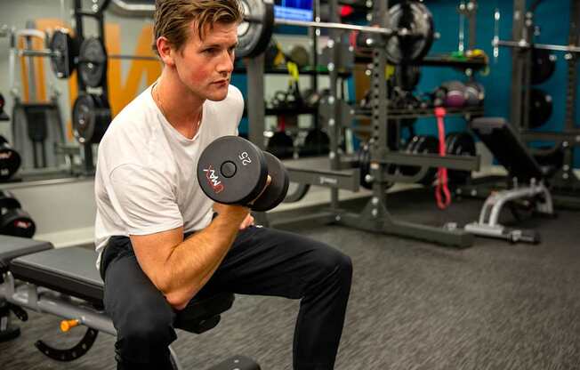 A man is sitting on a bench in a gym holding a dumbbell.