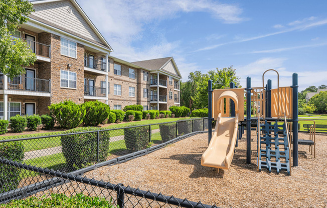 A playground with a slide and a climbing frame is in front of a building.