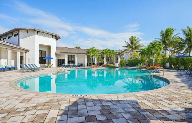 A swimming pool surrounded by a tiled patio and a white building with a balcony.