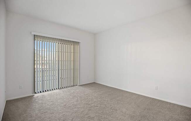 A room with a carpeted floor and a window with blinds.