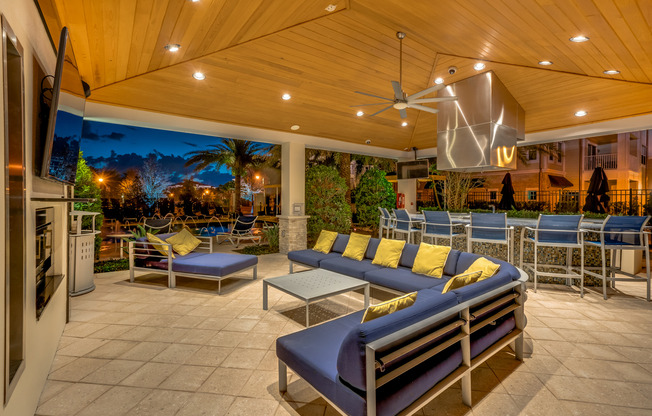 View of Grilling Lounge, Showing Pavilion Area, Outdoor Couch, TV, and Chairs in Circle Around Grill at The Marq Highland Park Apartments