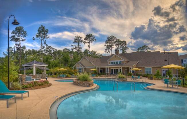 Resort-style swimming pool with lounge chairs with view of the resident clubhouse at Lullwater at Blair Stone apartments for rent in Tallahassee, FL