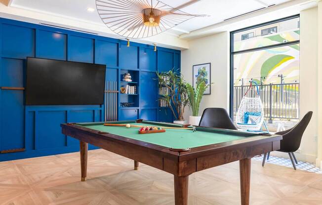 A pool table with a green felt cloth and a television on the wall.