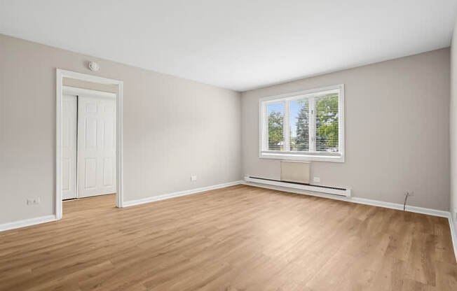 A room with a white door and a window with a view of trees.