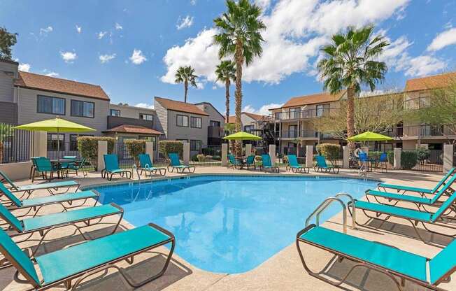 A pool surrounded by sun loungers and palm trees.