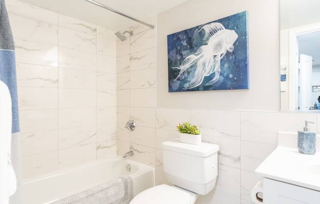 a bathroom with a white tub and toilet and a painting of a white jellyfish
