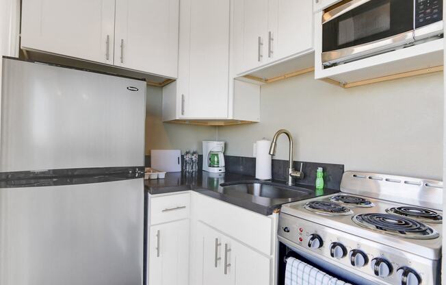 Studio Kitchen with Stainless Steel two door refrigerator, electric range, microwave, gray quartz countertops, white kitchen cabinets