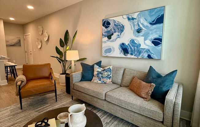 A living room with a grey couch, a brown armchair, a coffee table, and a large blue and white painting on the wall.