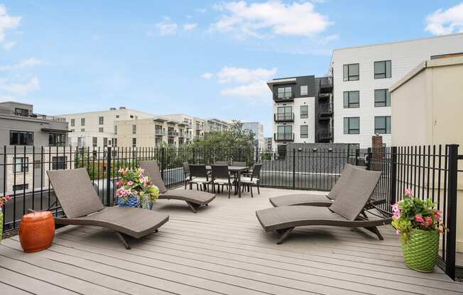 a rooftop deck with lounge chairs and a table with flowers