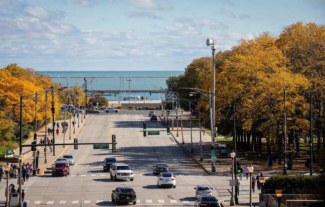 a city street with cars driving down it and the ocean in the distance