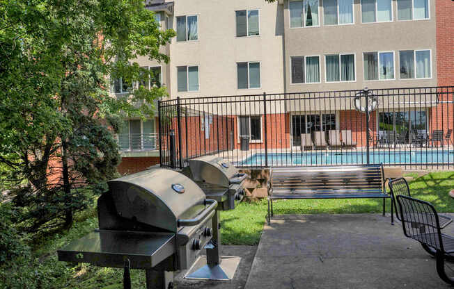 A BBQ grill is in the foreground of a courtyard with a pool and apartment building in the background.